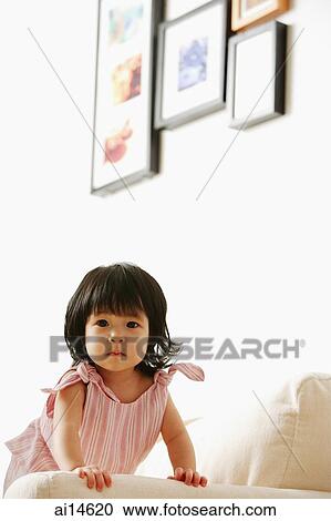 Stock Image - Baby girl on sofa, looking at camera. Fotosearch