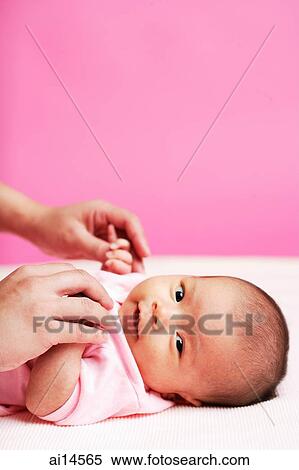 Stock Photography - Baby lying down, looking at camera, mother holding her hand. Fotosearch