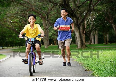 Stock Photo - Boy cycling, father running behind him. Fotosearch