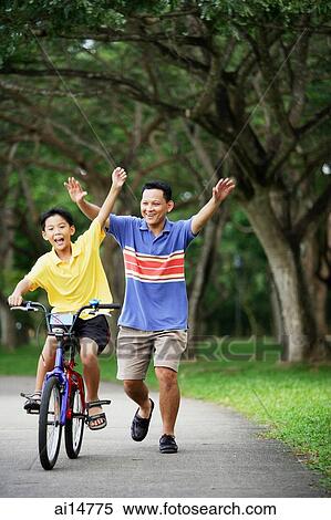 Boy on bicycle, father behind him, both with arms outstretched View Large Photo Image Stock Photography - Boy on bicycle, father behind him, both with arms outstretched. Fotosearch