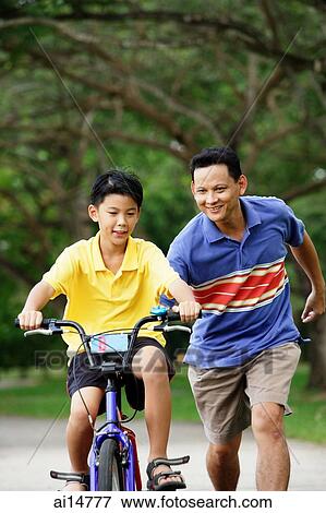 Stock Photo - Boy on bicycle, father running behind him. Fotosearch