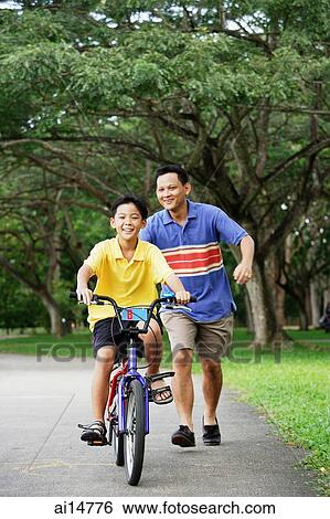 Boy on bicycle, father running behind him, smiling View Large Photo Image Stock Photograph - Boy on bicycle, father running behind him, smiling. Fotosearch