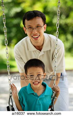 Stock Photo - Boy on swing, father behind him, both smiling at camera. Fotosearch