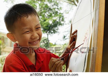 Stock Image - Boy painting on easel, smiling. Fotosearch