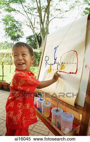 Boy pointing at drawing on easel, looking over shoulder, smiling View Large Photo Image Stock Photography - Boy pointing at drawing on easel, looking over shoulder, smiling. Fotosearch