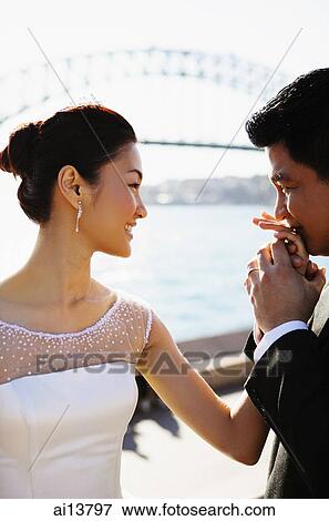 Bride and groom standing face to face, man kissing woman's hand View Large Photo Image Stock Photo - Bride and groom standing face to face, man kissing woman's hand. Fotosearch
