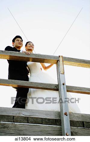 Picture - Bride and groom standing, hand on railing, looking away. Fotosearch