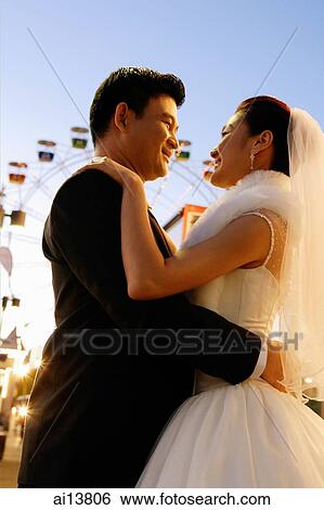 Stock Photograph - Bride and groom standing, looking at each other, Ferris wheel in the background. Fotosearch