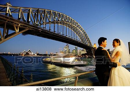 Stock Photo - Bride and groom standing, looking away, bridge and river in the background. Fotosearch