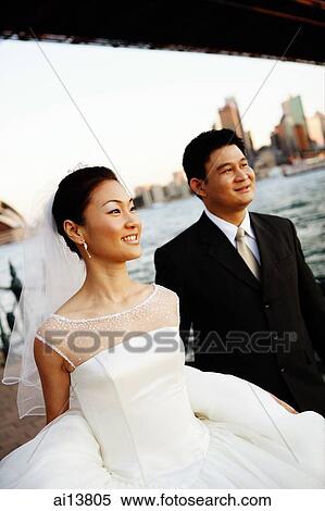 Stock Photography - Bride and groom standing, looking away, city and river in the background. Fotosearch