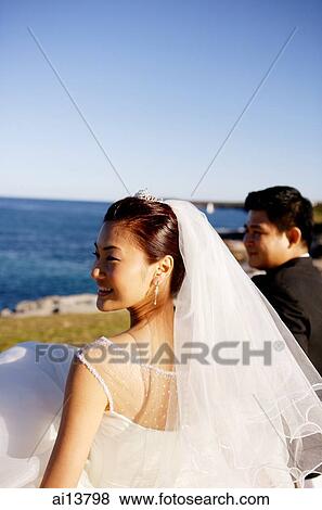Stock Photo - Bride and groom standing side by side, ocean in distance. Fotosearch