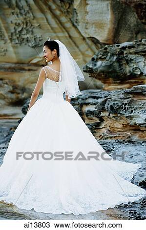Stock Image - Bride standing, looking away, rear view. Fotosearch
