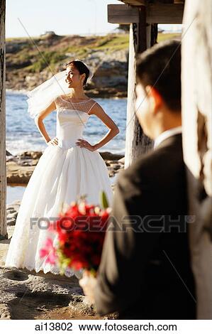 Stock Image - Bride standing with hands on hips, groom looking at her. Fotosearch