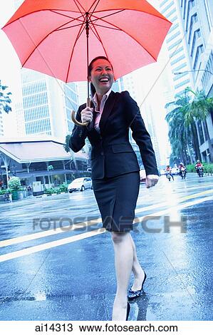 Stock Image - Business woman holding umbrella, walking across the road. Fotosearch