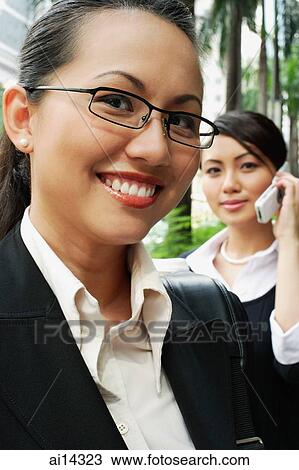 Stock Image - Business woman, smiling, looking at camera, woman in the background on the phone. Fotosearch