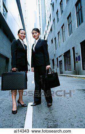 Stock Image - Business women standing side by side looking at camera, portrait. Fotosearch