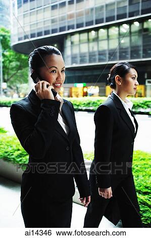 Business women walking side by side, one on the phone View Large Photo Image Stock Photograph - Business women walking side by side, one on the phone. Fotosearch