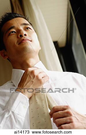 Stock Image - Businessman fixing tie, low angle view. Fotosearch