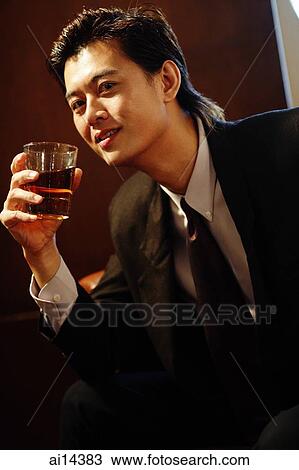 Stock Image - Businessman holding glass of whiskey, looking at camera. Fotosearch