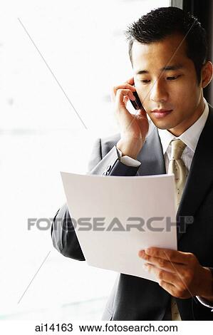 Businessman looking at document, using mobile phone View Large Photo Image Stock Image - Businessman looking at document, using mobile phone. Fotosearch