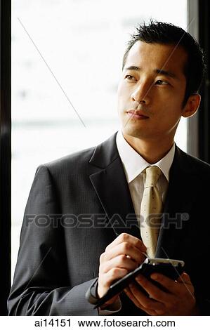 Stock Image - Businessman looking away, holding PDA. Fotosearch