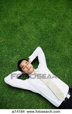 Picture - Businessman lying on grass, hands behind head, eyes closed. Fotosearch
