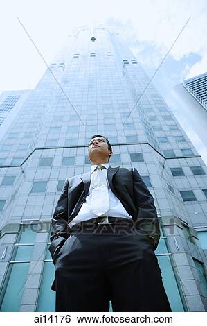 Businessman with hands in his pocket, building in the background View Large Photo Image Stock Photograph - Businessman with hands in his pocket, building in the background. Fotosearch