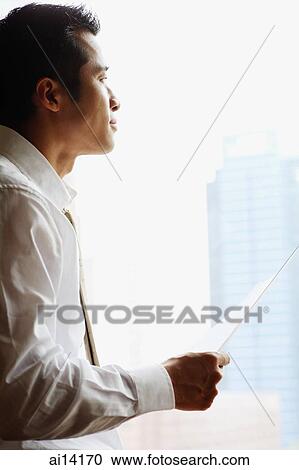 Stock Image - Businessman with holding paper, looking away, sideview. Fotosearch