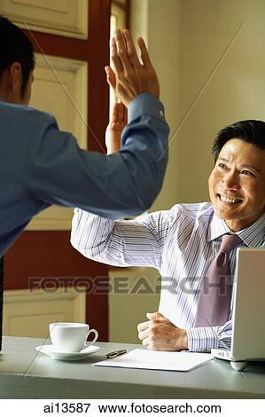 Businessmen giving high five over desk View Large Photo Image Stock Photo - Businessmen giving high five over desk. Fotosearch
