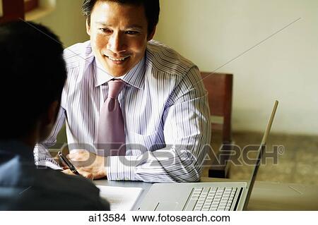 Picture - Businessmen talking, laptop open next to them. Fotosearch