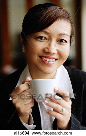 Picture - Businesswoman holding cup, looking at camera. Fotosearch