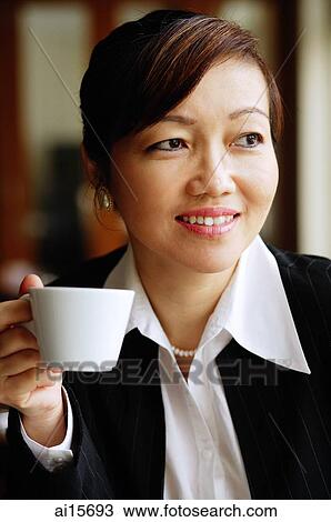 Stock Image - Businesswoman holding cup, looking away. Fotosearch