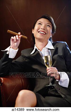 Businesswoman holding glass of champagne and cigar, looking up View Large Photo Image Stock Photo - Businesswoman holding glass of champagne and cigar, looking up. Fotosearch