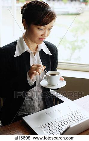 Stock Photo - Businesswoman looking at laptop, holding cup and saucer. Fotosearch