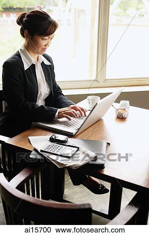 Stock Image - Businesswoman sitting at table using laptop. Fotosearch