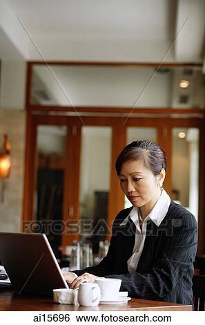 Stock Photograph - Businesswoman sitting at table using laptop. Fotosearch