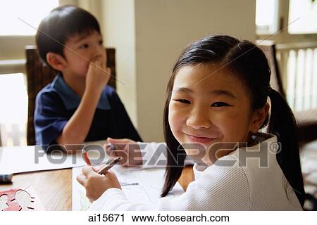 Stock Image - Children sitting at table, girl turning to smile at camera. Fotosearch