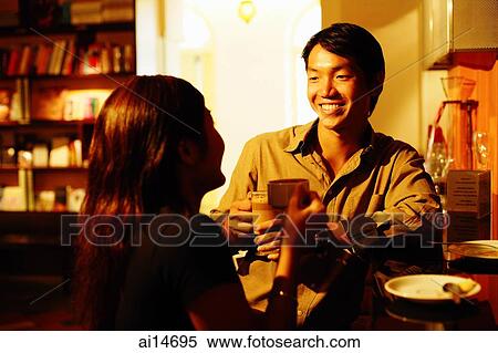 Couple at bar counter, holding coffee cups, talking View Large Photo Image Stock Photography - Couple at bar counter, holding coffee cups, talking. Fotosearch