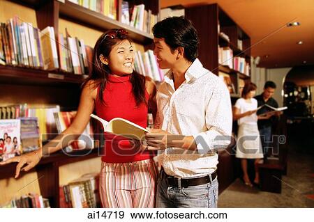 Couple at bookstore, looking each other, man holding book View Large Photo Image Stock Photo - Couple at bookstore, looking each other, man holding book. Fotosearch