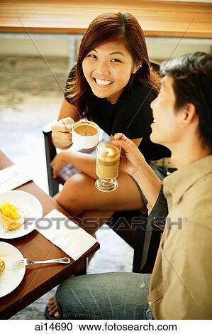Stock Image - Couple at cafe, holding cups of coffee, woman looking up at camera. Fotosearch