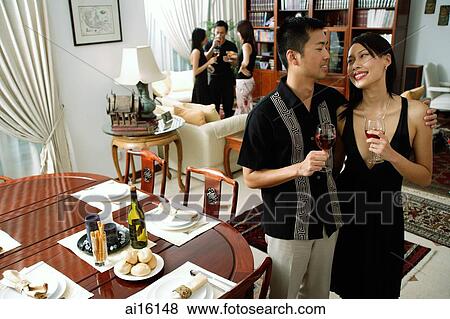 Couple at home, holding wine glasses, smiling at each other, people in the background View Large Photo Image Stock Photo - Couple at home, holding wine glasses, smiling at each other, people in the background. Fotosearch