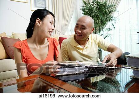 Couple at home in living room, looking at each other, photo album in front of them View Large Photo Image Stock Photo - Couple at home in living room, looking at each other, photo album in front of them. Fotosearch