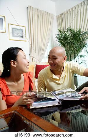 Couple at home in living room, photo album in front of them View Large Photo Image Stock Photo - Couple at home in living room, photo album in front of them. Fotosearch