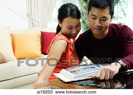 Stock Image - Couple at home, looking at photo album in front of them. Fotosearch