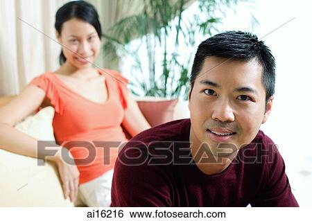 Couple at home, man looking at camera, smiling, woman sitting in the background View Large Photo Image Stock Photograph - Couple at home, man looking at camera, smiling, woman sitting in the background. Fotosearch