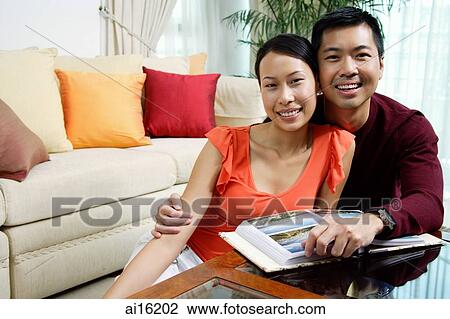 Stock Image - Couple at home, smiling at camera photo album in front of them. Fotosearch