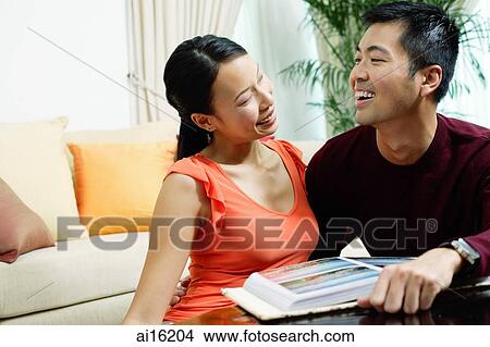 Couple at home, smiling at each other, photo album in front of them View Large Photo Image Picture - Couple at home, smiling at each other, photo album in front of them. Fotosearch