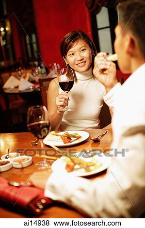 Couple at restaurant, woman holding wine glass, man eating View Large Photo Image Stock Photo - Couple at restaurant, woman holding wine glass, man eating. Fotosearch