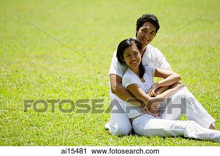Couple embracing, sitting on grass, smiling at camera View Large Photo Image Stock Image - Couple embracing, sitting on grass, smiling at camera. Fotosearch