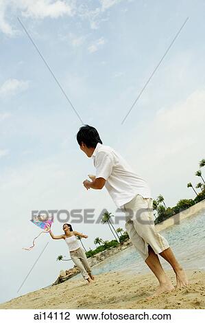 Stock Image - Couple flying kite along beach, man turning to look at woman. Fotosearch